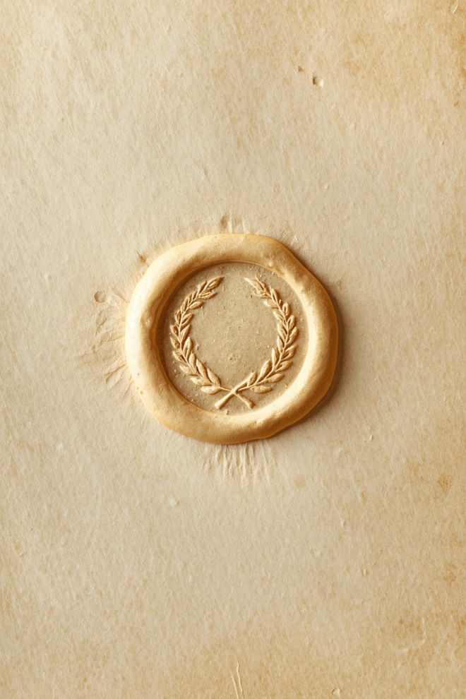 A gold wax seal pressed with a laurel wreath on cream paper.
